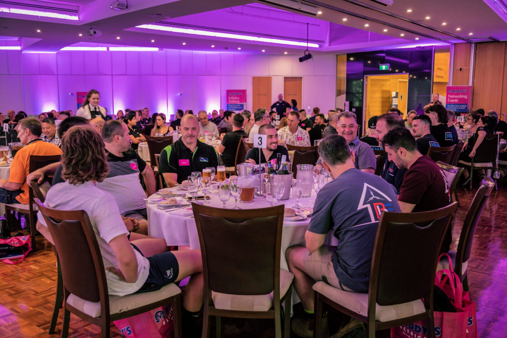 A group of people sitting at tables in front of purple lights.